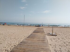 Une plage de sable avec une promenade en bois menant à l’eau, des empreintes de pas et un poste de surveillance pour les sauveteurs.