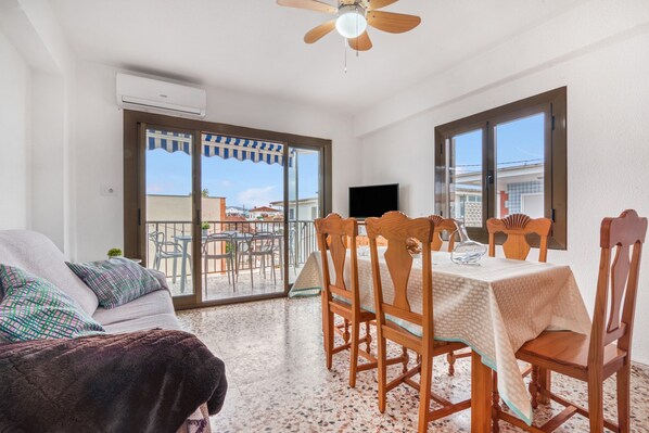 Una habitación con sofá, una mesa de comedor con sillas, un ventilador de techo y televisión.