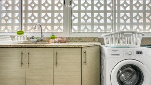 A kitchen with a washing machine, a sink, and a window with a decorative screen.