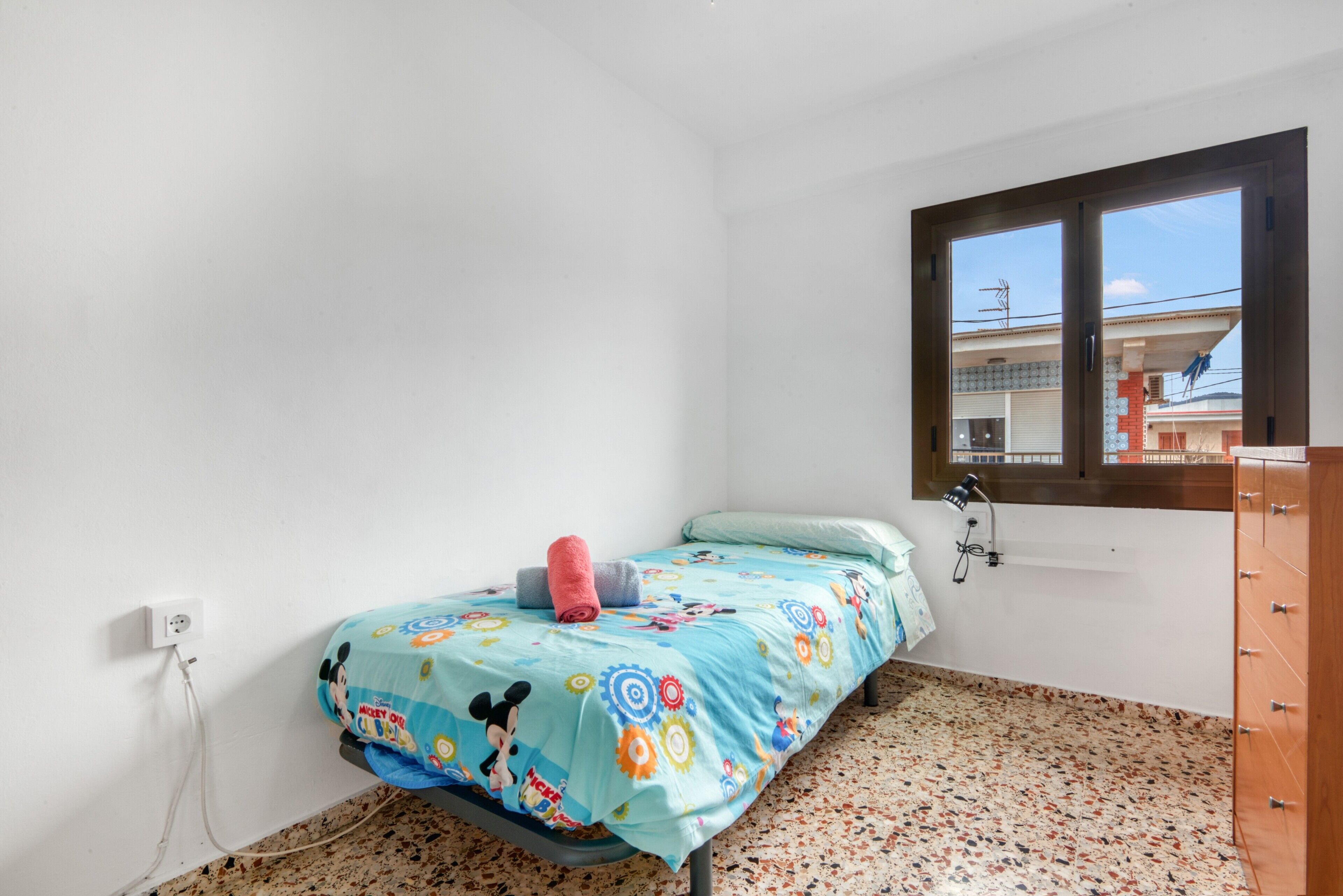 Un dormitorio con cama, ventana, cómoda y toma de corriente.