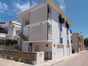 Un edificio de dos pisos con fachada blanca, un balcón con diseño geométrico y una puerta de garaje.