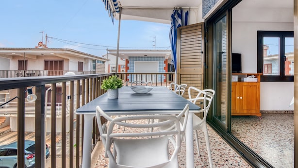 A balcony with a table and chairs, a potted plant, a wooden cabinet, and a view of the street.