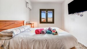 A bedroom with a bed, a window, a TV, and a small table.