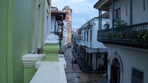 Une rue étroite, bordée de bâtiments des deux côtés, un clocher visible au loin, et une personne qui marche dans la rue.