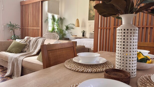 Un coin repas chaleureux avec une table en bois, des sets de table en fibres naturelles et un vase blanc orné d’une plante.