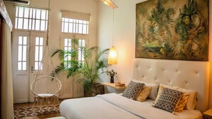 Une chambre à coucher avec un lit, un fauteuil suspendu, une plante en pot et une œuvre d’art accrochée au mur.