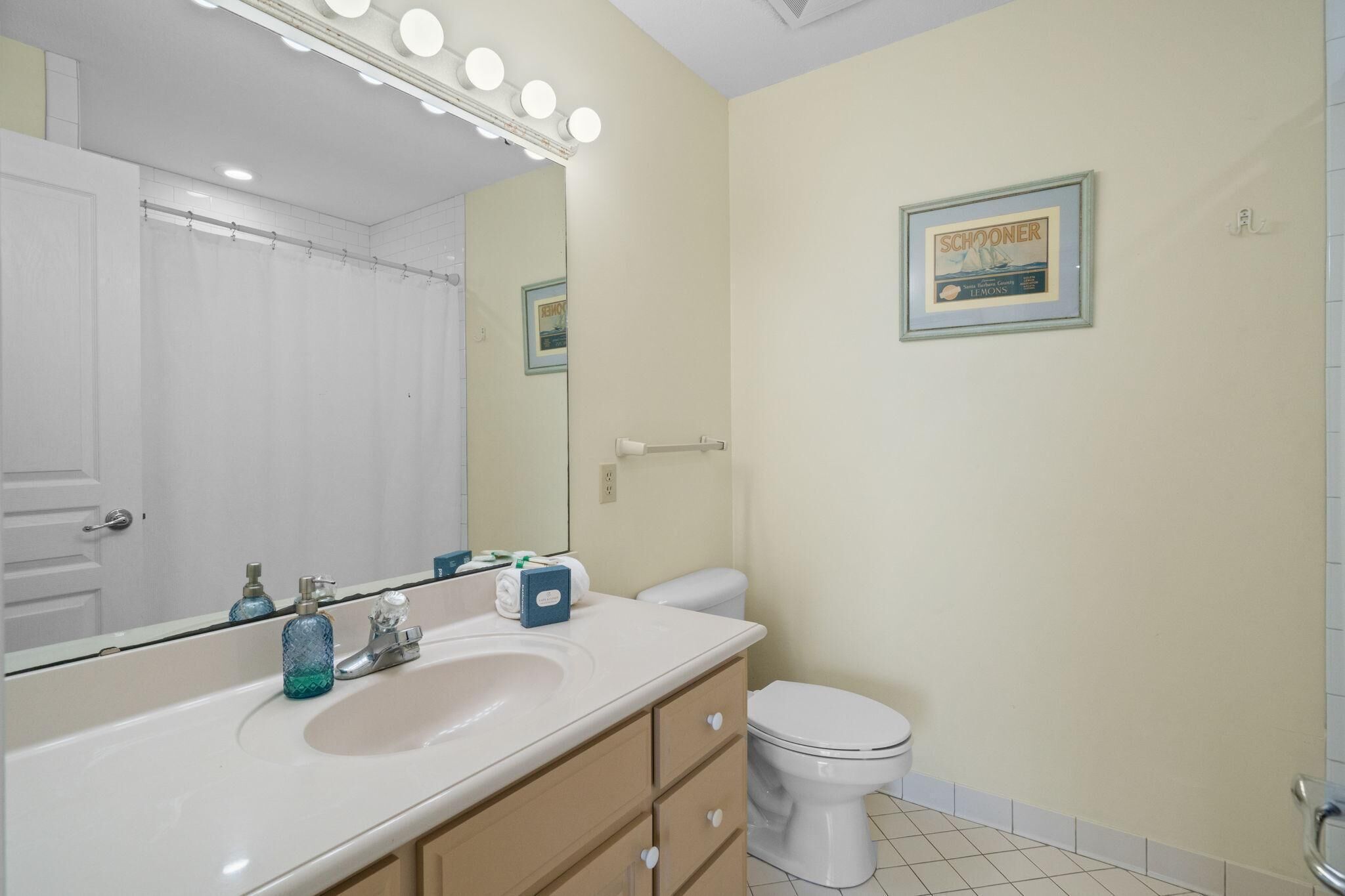 Ein Badezimmer mit Waschbecken, Spiegel und Toilette. Über dem Spiegel befinden sich Lampen und ein gerahmtes Bild an der Wand.