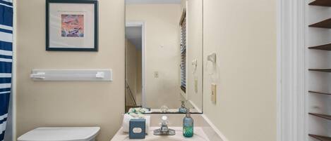 A bathroom with a white sink, a framed picture on the wall, and a mirror with lights above it.