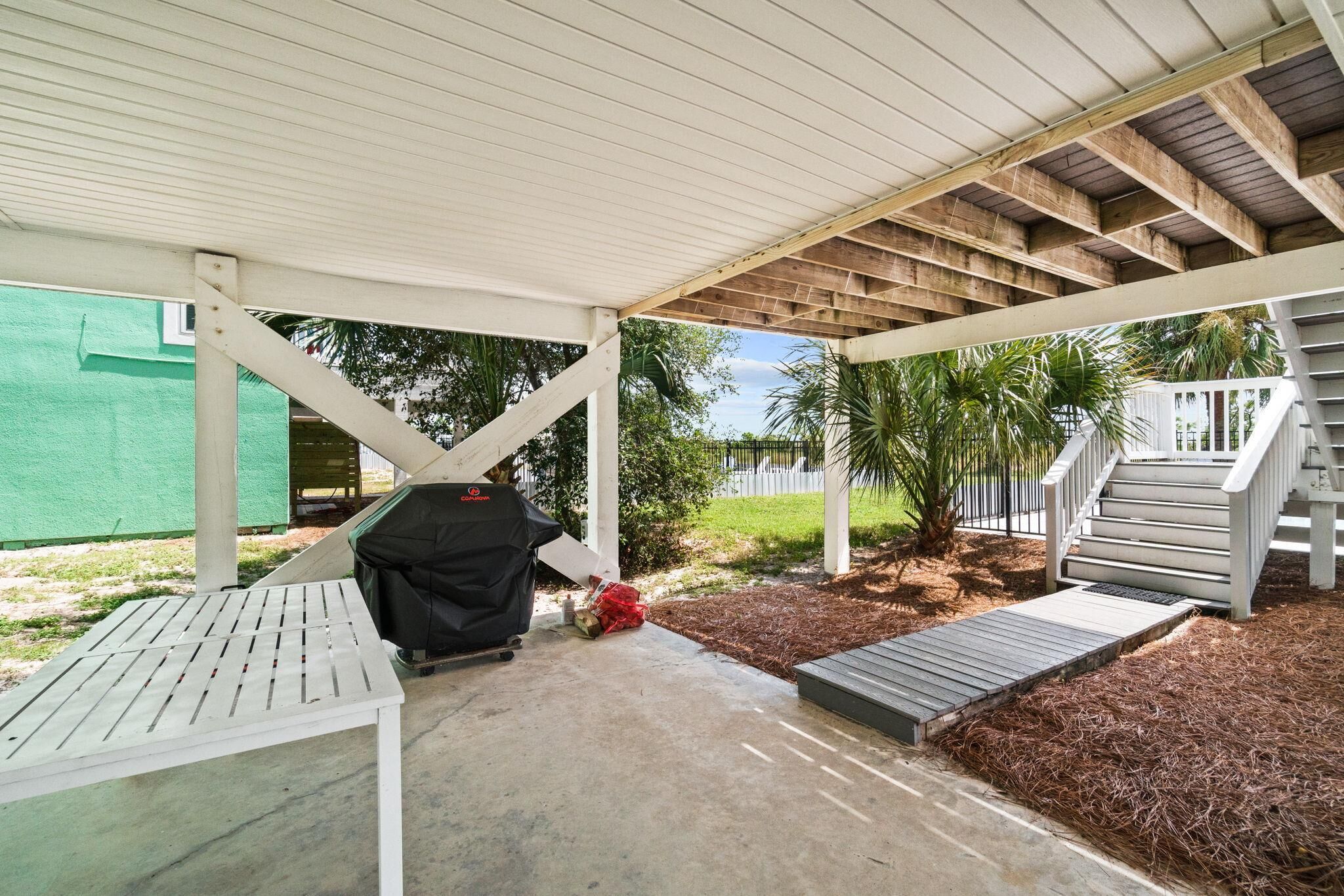 A covered patio area with a grill, a table, and a small ramp leading to a deck.