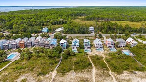 Luchtbeeld van een kustresort met meerdere bungalowachtige gebouwen, een zwembad en een strand.