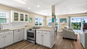 A modern kitchen with white cabinetry, a central island, and a dining area with a gray sofa.