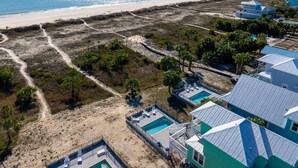 An aerial view of a coastal property with a beach, pathways, and a swimming pool area.