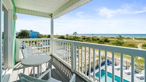 A covered outdoor area with a pool, white railings, and a view of the beach.
