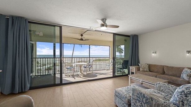 A spacious balcony with a view of the beach, a ceiling fan, and a sofa with patterned cushions. - Mariners Boathouse by Coolvacay (Fort Myers Beach)