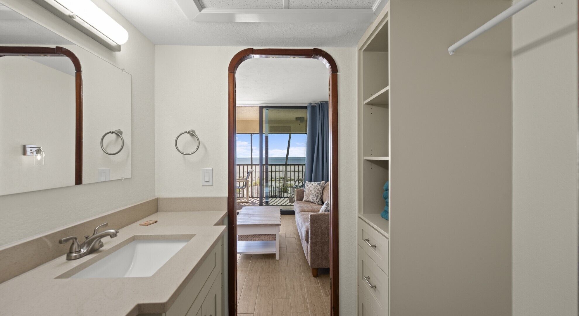 A modern bathroom with a large mirror, a sink, and a shower. There is a balcony with a view of the beach.