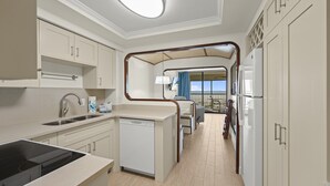 Een compacte keuken met een ingebouwde vaatwasser, een spoelbak en een fornuis. Er is een balkon met uitzicht op zee.