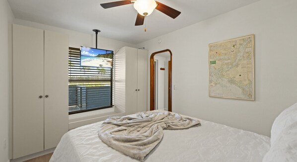 A bedroom with a bed, a ceiling fan, a window with blinds, a map on the wall, and a wardrobe. - Mariners Boathouse by Coolvacay (Fort Myers Beach)