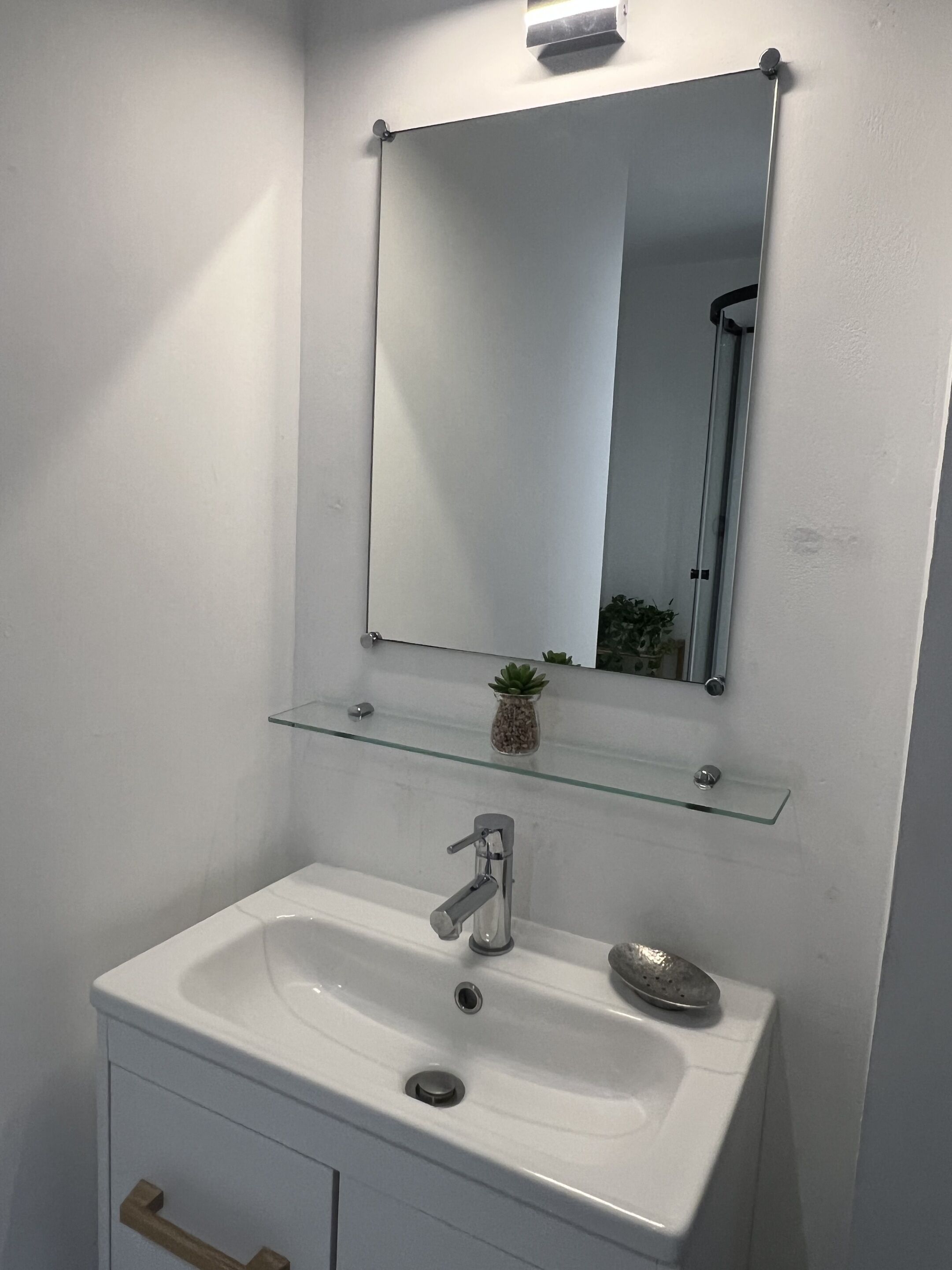 A bathroom with a white sink, a glass shelf above it, and a mirror.