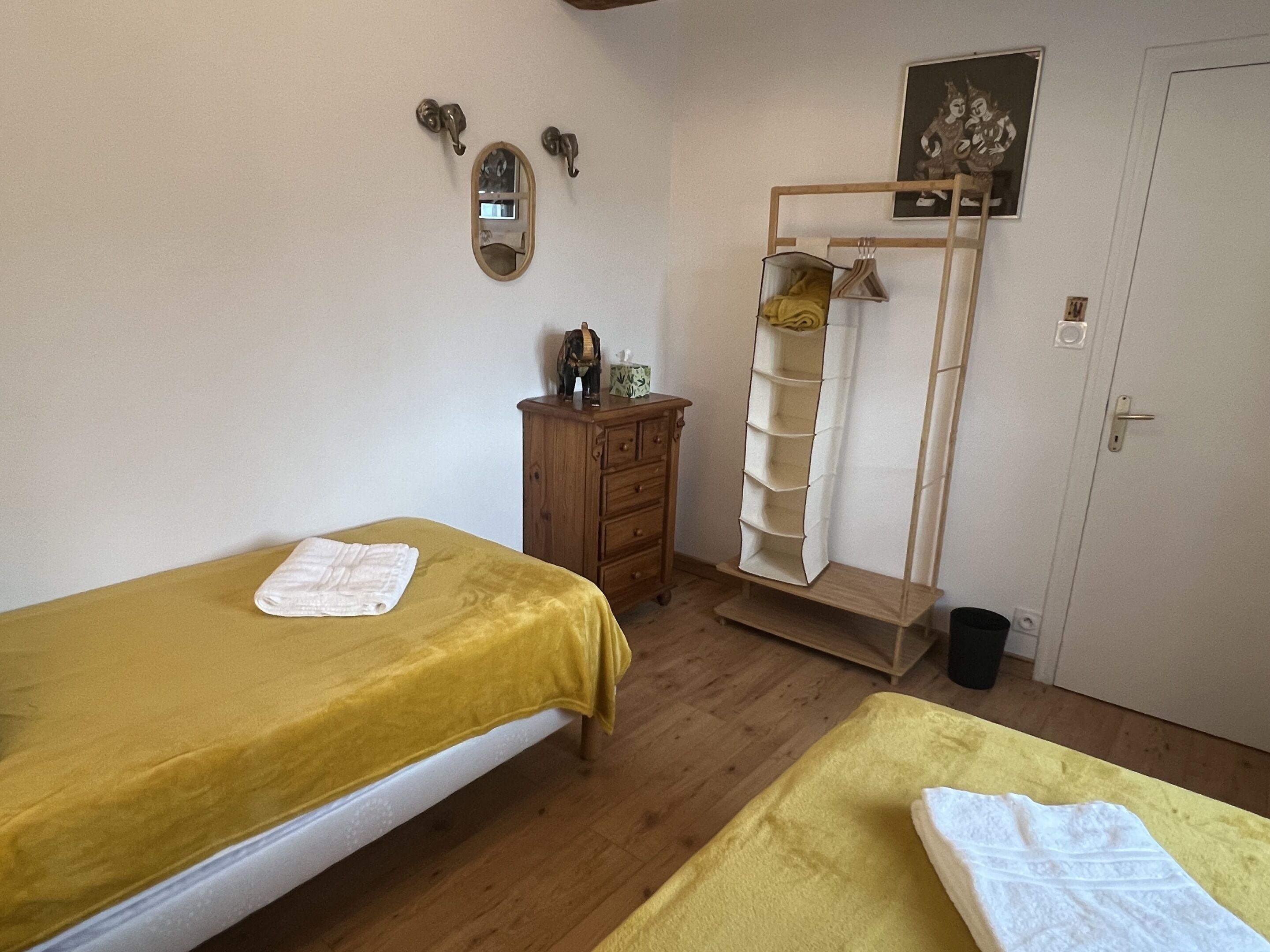 Una habitación con dos camas, un aparador de madera, una estantería y una puerta con un cuadro encima.