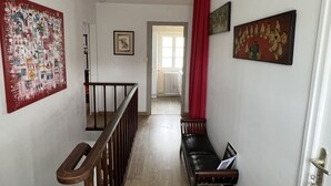 A hallway with a wooden staircase, a bench, and artwork on the walls. - Au pré du Puy (Chanverrie)