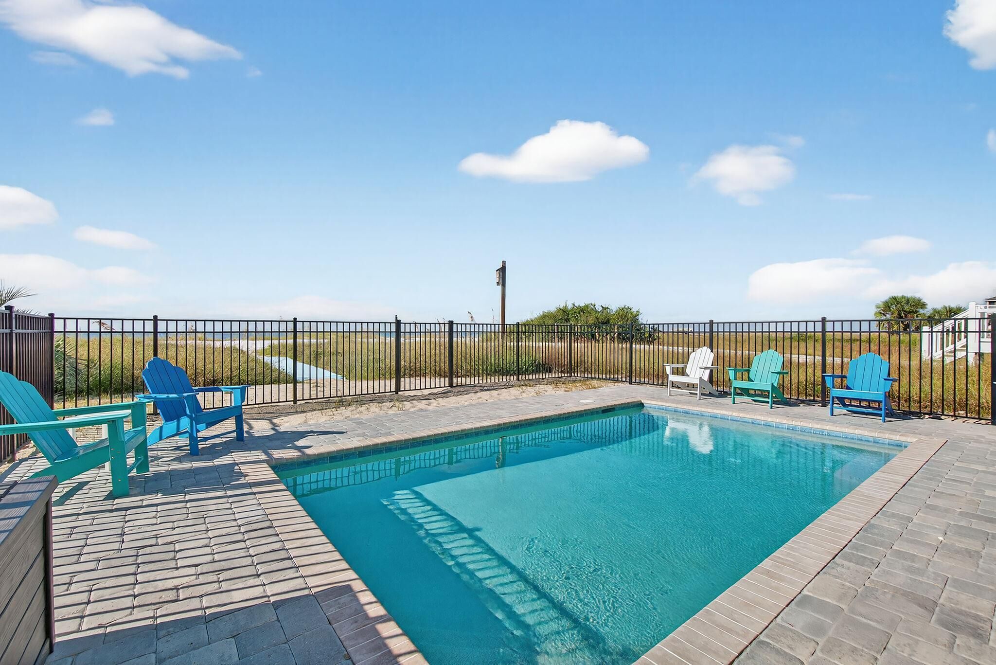 A swimming pool with a brick deck, surrounded by a black metal fence.