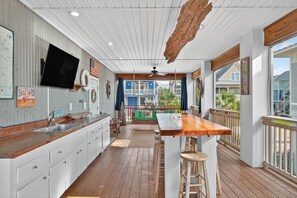 Eine Küchentheke im maritimen Stil mit einer Holztresore, weißen Schränken und einem großen Fenster mit Blick auf ein blaues Gebäude.