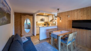 Een gezellige woonkamer met een bank, een eettafel met stoelen, een keuken met een magnetron en een aan de muur bevestigde televisie.