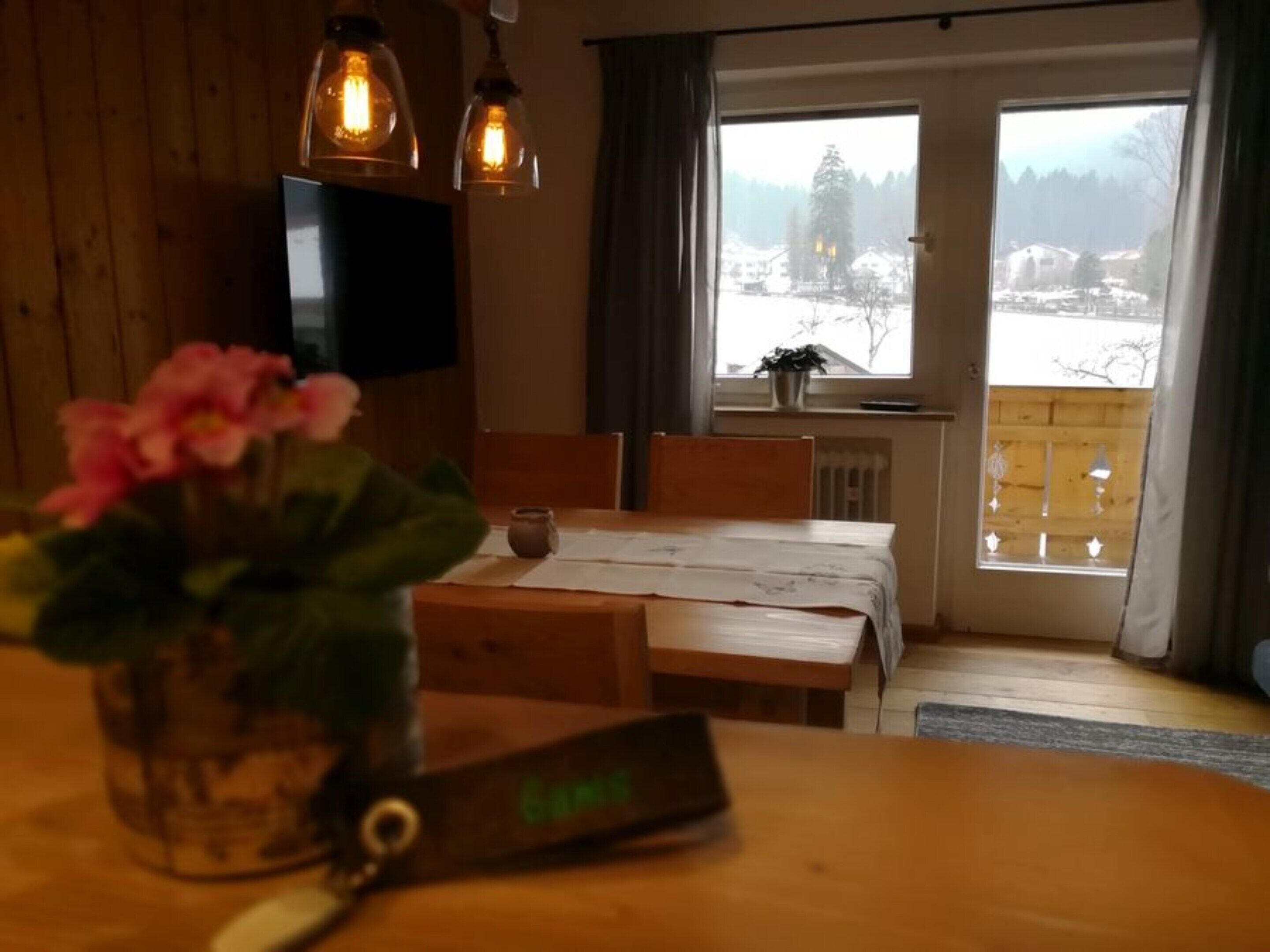Una habitación acogedora con una mesa de madera, un televisor montado en la pared y vistas a un paisaje nevado a través de la ventana.