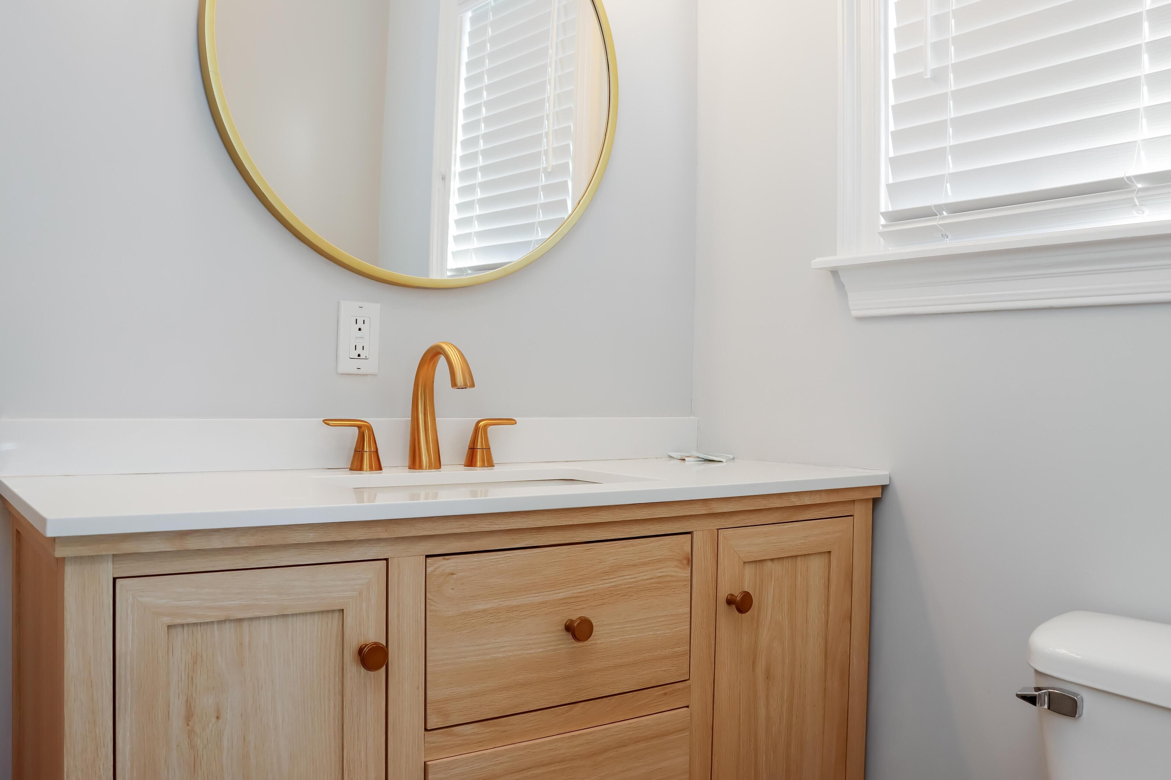 A bathroom with a white sink, gold faucets, and wooden cabinets.