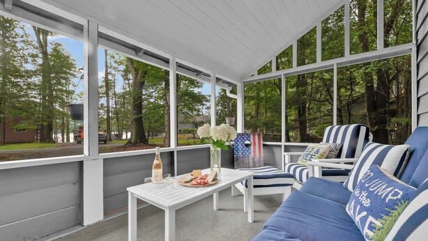 A covered patio with a white table set with food and drinks, striped blue and white outdoor furniture, and a view of trees and a house in the background.