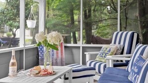 A covered outdoor seating area with striped chairs and a table set for dining, overlooking a forested area.