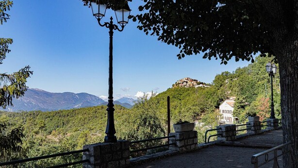 A paved pathway with stone railings, leading to a hilltop view of a white building with a red roof, surrounded by lush greenery and mountains in the background. - Between sea and mountains, pets welcome, hiking, walks from the house (Revest-les-Roches)