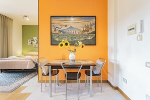 A hotel room with a bed, a dining table with chairs, a painting on the wall, and a vase with flowers. - Elegant panoramic openspace a few steps from the sea (Quartu Sant'Elena)