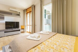 A hotel room with a bed, a TV, a desk, and a bathroom visible through the window. - Elegant panoramic openspace a few steps from the sea (Quartu Sant'Elena)