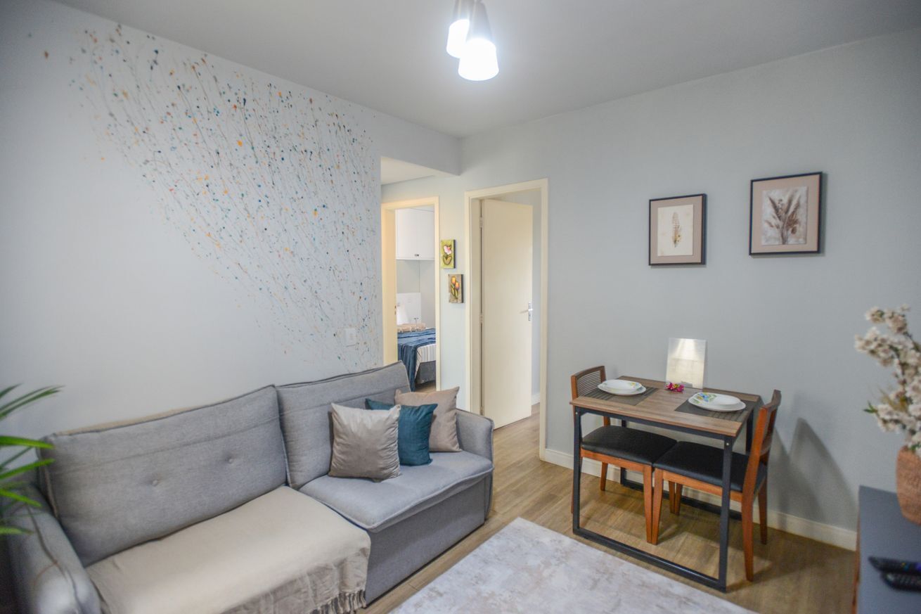 Un salon avec un canapé gris, une table à manger avec des chaises et un mur orné d’œuvres d’art abstraites.