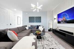 A modern living room with a sectional sofa, a round coffee table, and a flat-screen TV mounted on the wall. - Spacious Solara Resort Home, Near Disney, 4BR, Private Pool, Sleeps up to 12 (Kissimmee)