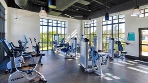 Una palestra con macchinari cardio, postazioni per pesi e ampie finestre che offrono luce naturale.