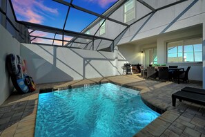 An indoor swimming pool with a view of the sky through a glass ceiling, a patio area with outdoor furniture, and a small table with chairs. - Spacious Solara Resort Home, Near Disney, 4BR, Private Pool, Sleeps up to 12 (Kissimmee)