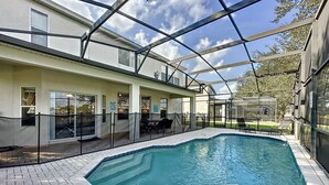 Ein Schwimmbecken mit Glasumrandung, umgeben von einer Terrassenfläche mit Stühlen und Tischen.
