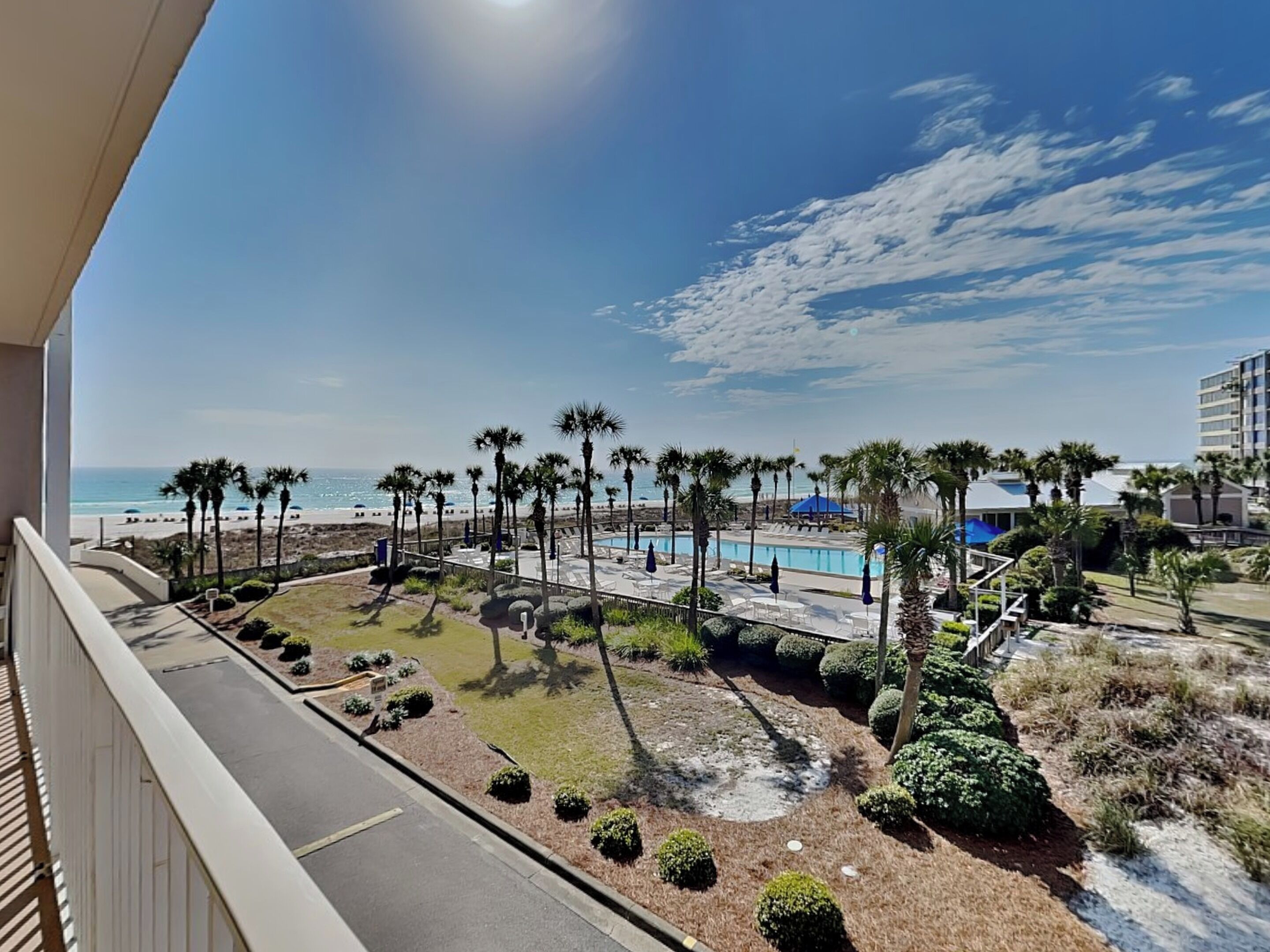 Ein Balkon mit Blick auf einen Strand, Palmen und einen Poolbereich.