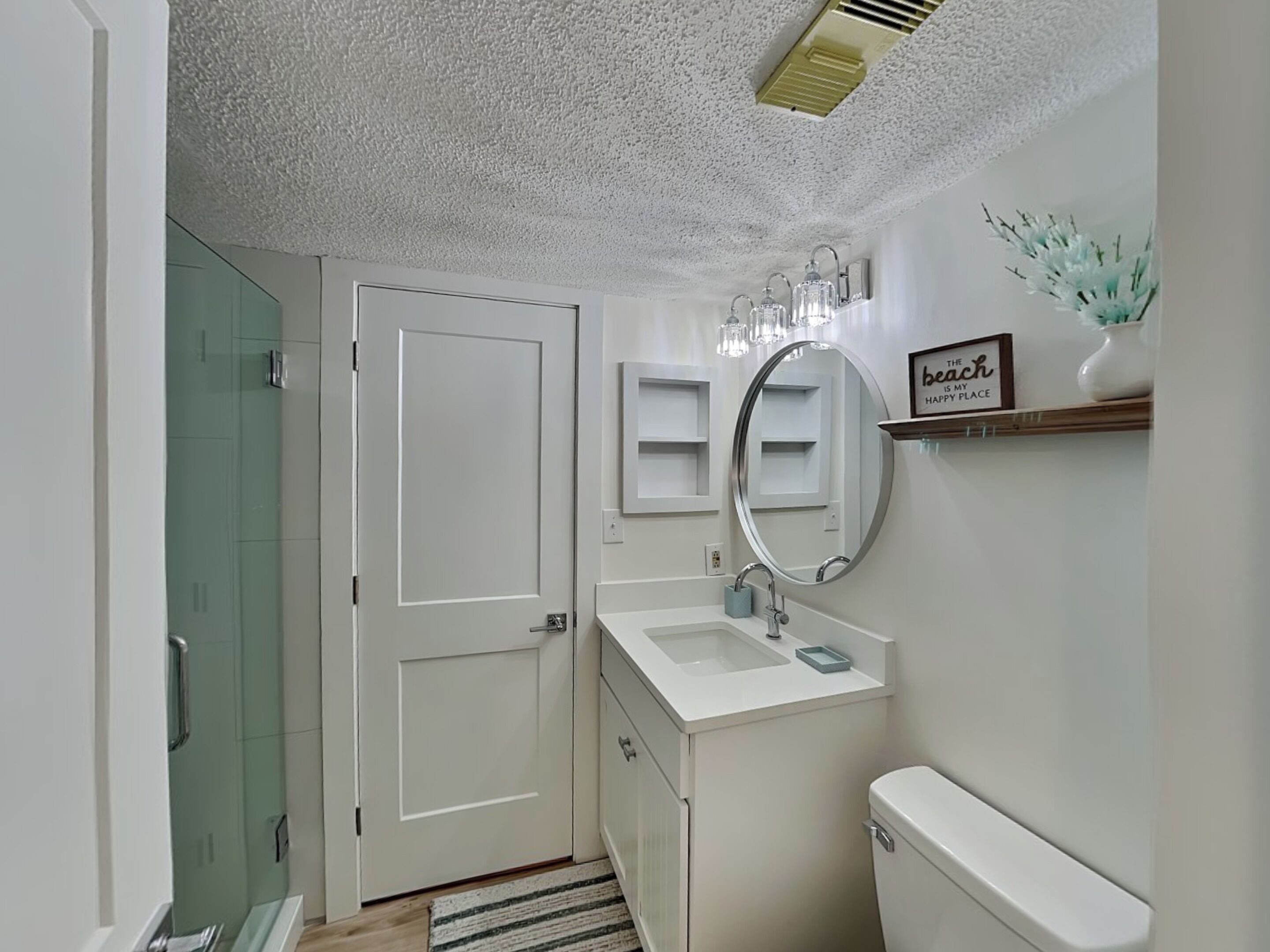 A bathroom with a white sink, a toilet, a shower, and a door.