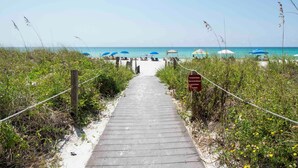 A wooden boardwalk leading to a beach with blue umbrellas and beach chairs. - Dunes of Panama #c503 (Panama City Beach)