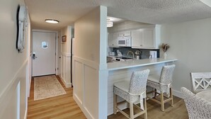 A compact kitchen with white cabinets, a microwave, and a sink. There are two wicker chairs and a small dining table. - Dunes of Panama #c503 (Panama City Beach)