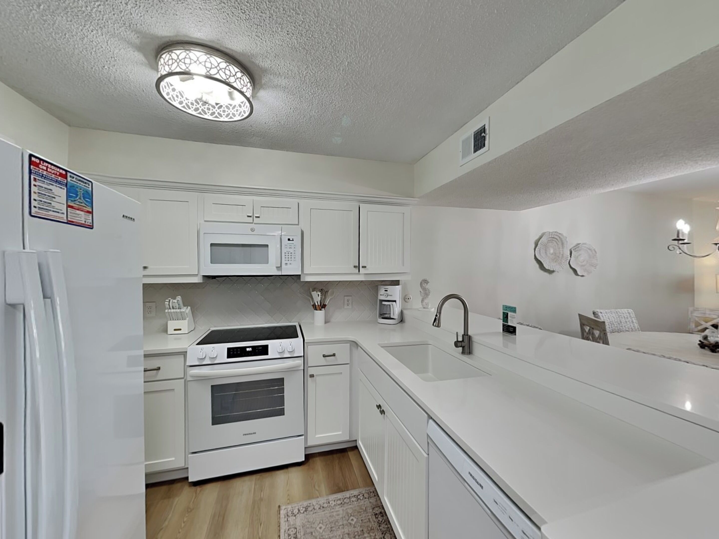 A modern kitchen with white cabinetry, a built-in oven, a microwave, a sink, and a coffee maker.