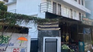 A two-story building with a gated entrance and a small shop selling vegetables. - vhost - 1 Twin room (Aluva)