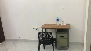 A small, clean room with a wooden desk, a black chair with a unique pattern, a water bottle, and a glass on the desk. - vhost - 1 Twin room (Aluva)