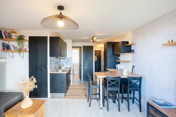 A modern kitchen with dark cabinets, a dining area with a wooden table and chairs, and a living area with a sofa and a decorative vase.