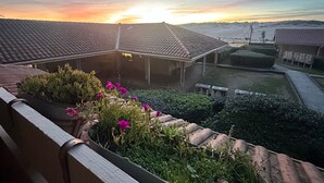 A courtyard with a tiled roof, a flower bed with pink flowers, and a view of the sunset.