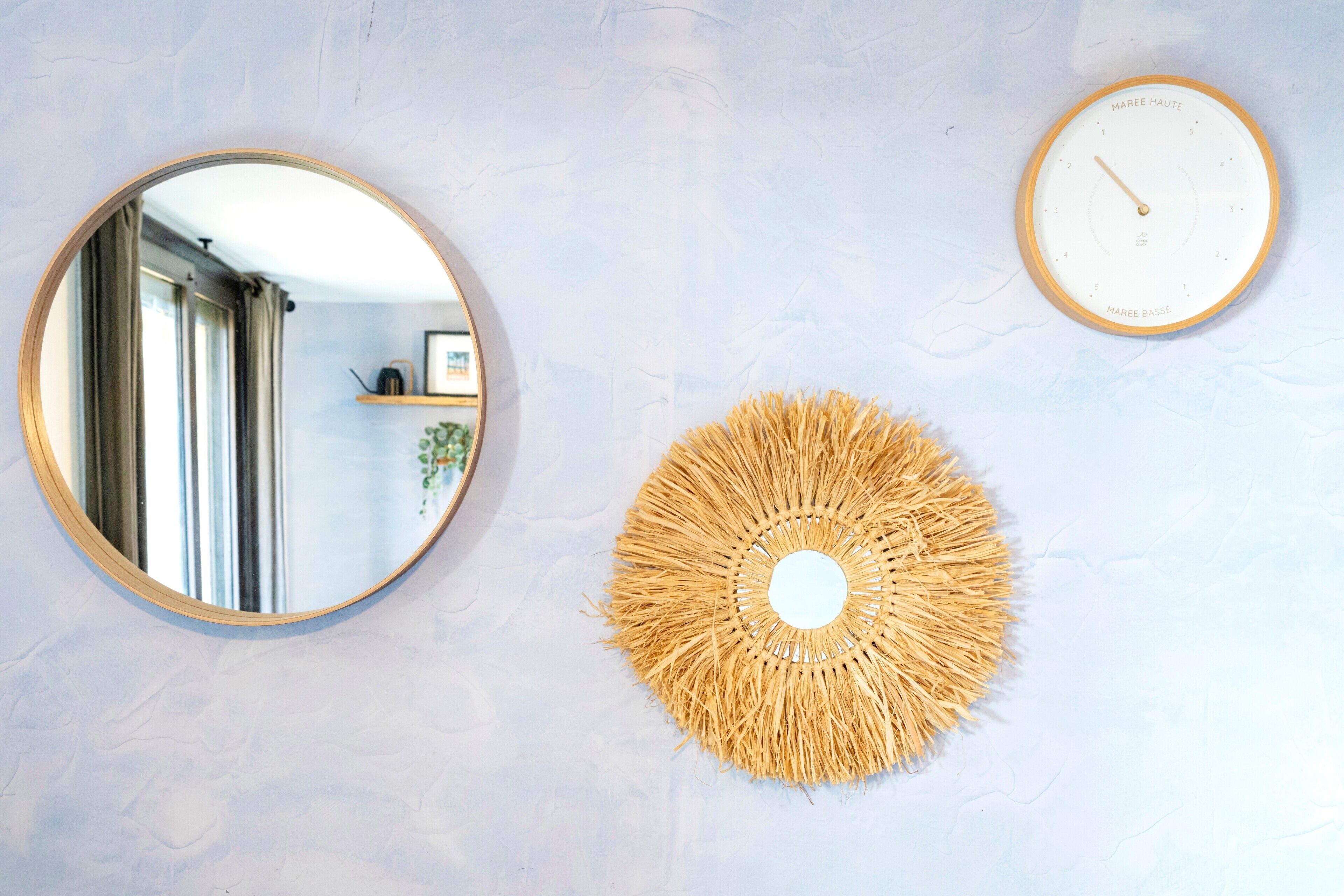 A wall with a round mirror, a clock, and a woven wall decoration.