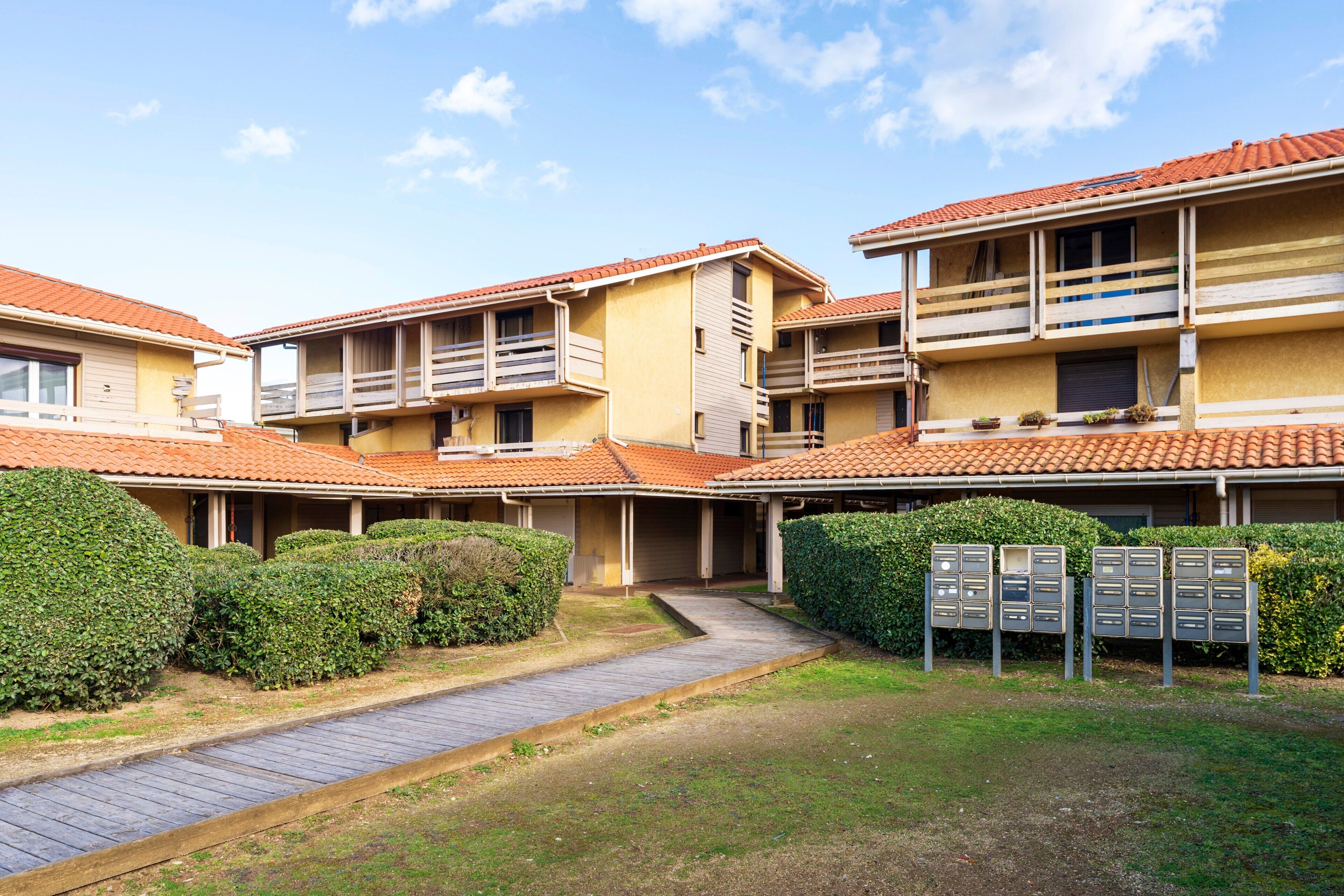 A residential building with multiple balconies, a paved walkway, and a mailbox area.